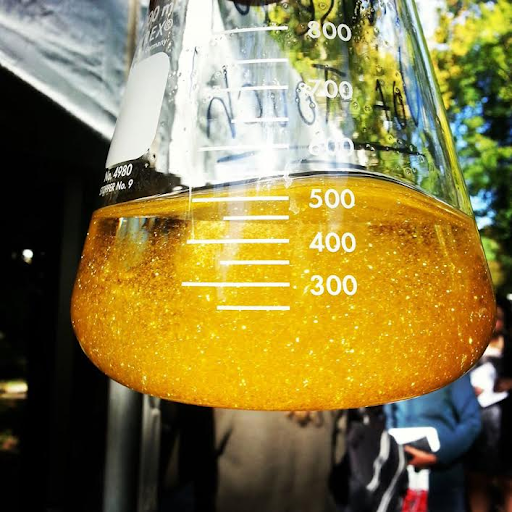 Stock image of an orangey-yellow sparkly solution in a clear glass flask, top of flask is cut off from photo.